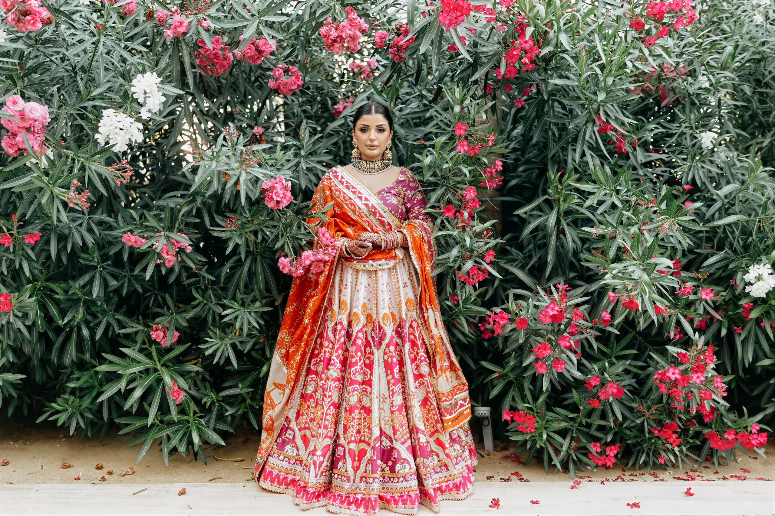 Bride in a vibrant lehenga standing in a garden setting after final wedding styling and preparation.