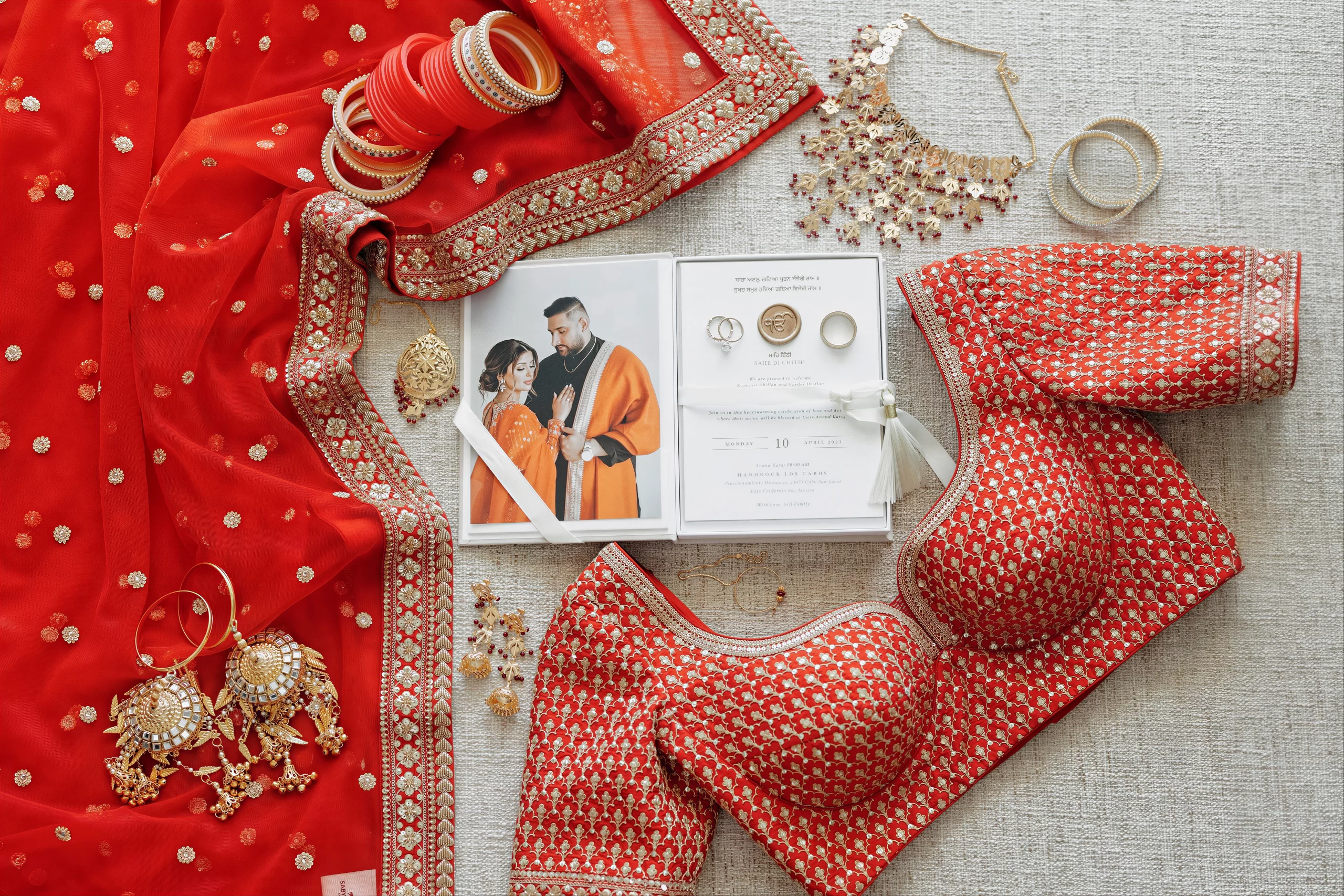 Flat lay of bridal styling elements including a red bridal dupatta, jewellery, bangles, and wedding invitation during style consultation planning.