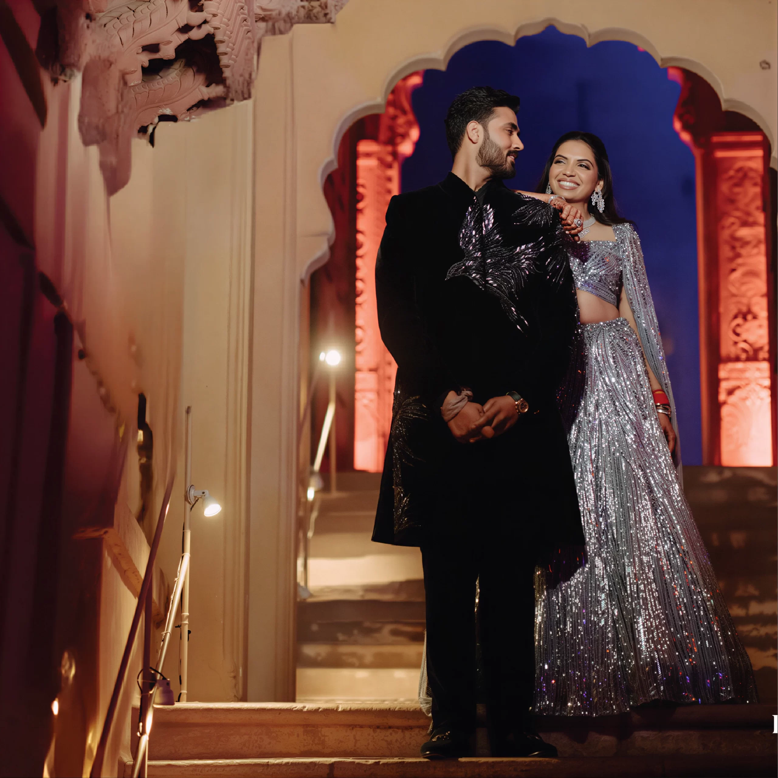 Groom wearing black sherwani styled for wedding reception with bride in silver lehenga